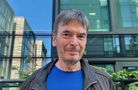 Ian Rankin smiling at the camera outside some flats