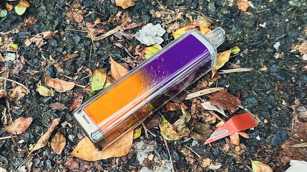 A discarded orange and purple disposable vape lies on the ground