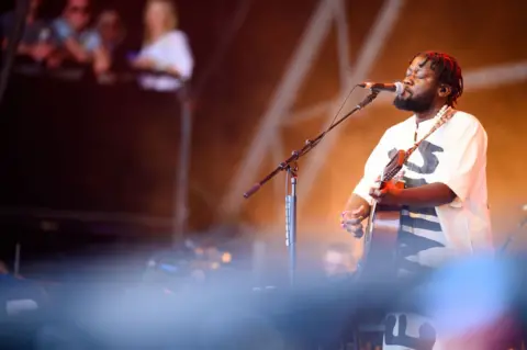 Getty Images Michael Kiwanuka, dressed in a Ugandan Kunzu, plays on the Pyramid Stage at the Glastonbury Festival in June 2024.