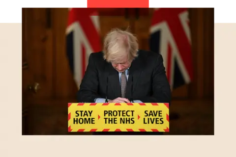 Getty Images Boris Johnson looks down at the podium as he attends a virtual press conference on the Covid-19 pandemic, the slogan on the stage reads 'stay home, protect the NHS, save lives'